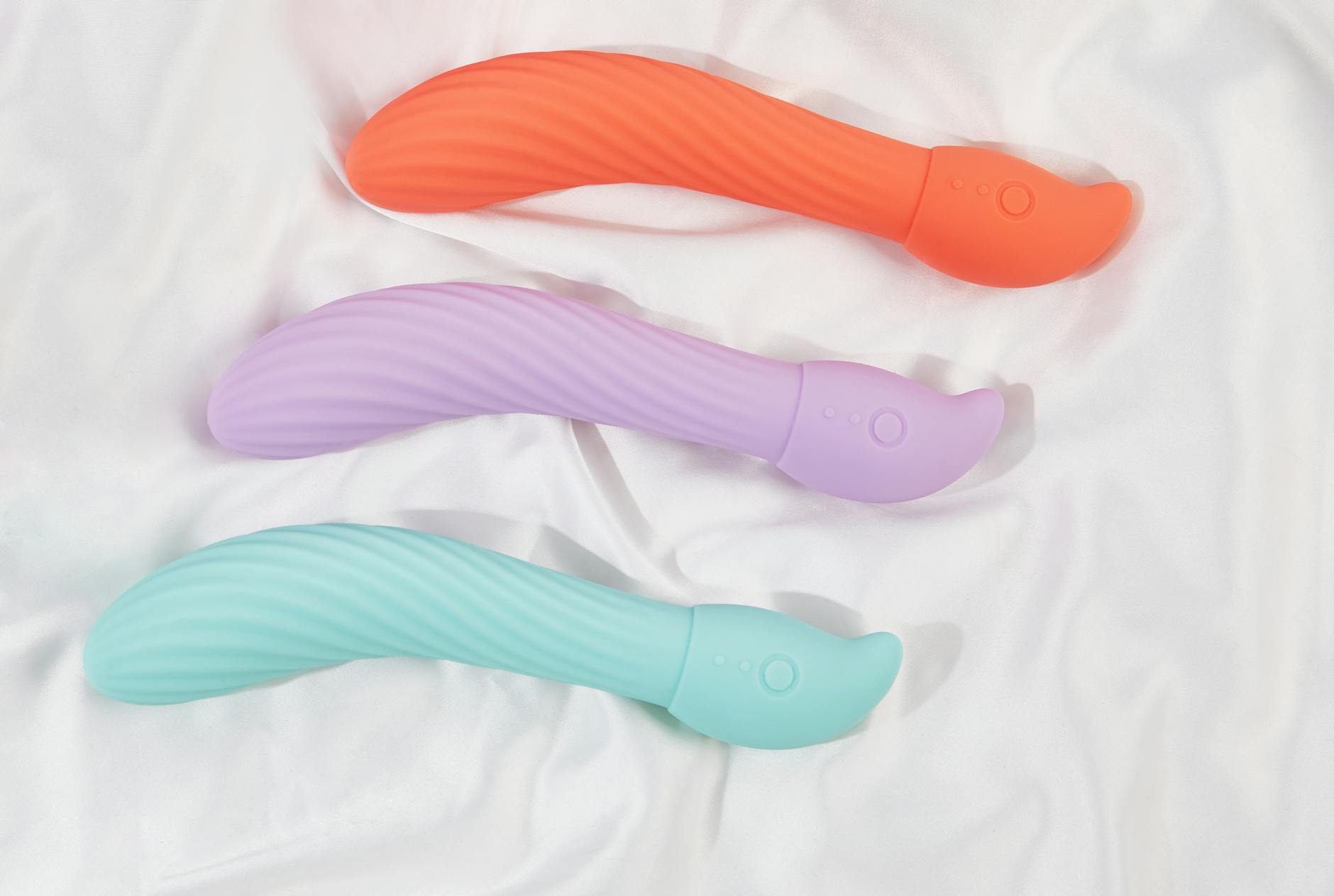 Three colorful clitoral vibrators arranged on white fabric, highlighting smooth texture and modern design