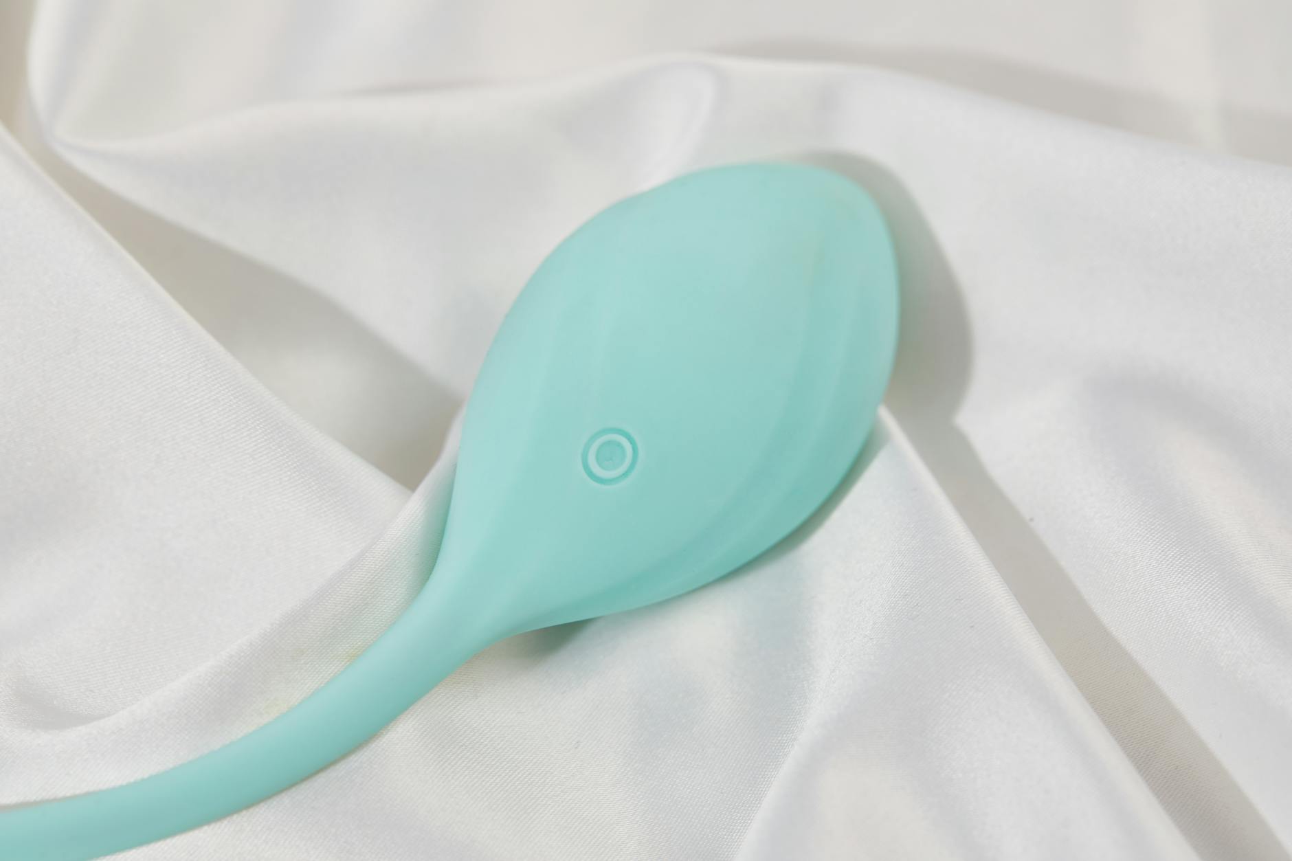 A stylish teal vibrator on smooth white silk fabric, perfect for intimate moments.