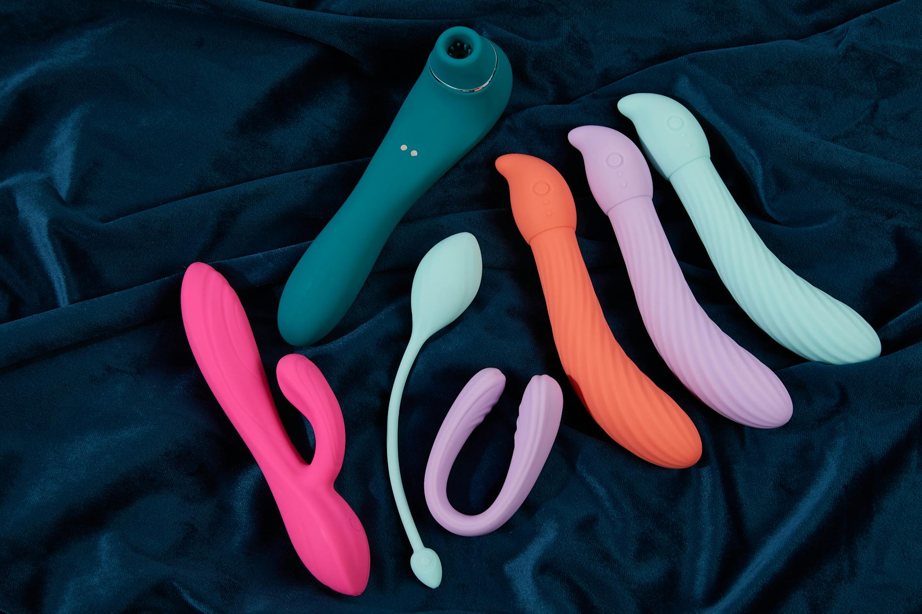 Vibrant display of colorful silicone sex toys on dark blue fabric, showcasing various shapes including a lemon-shaped clitoral vibrator.