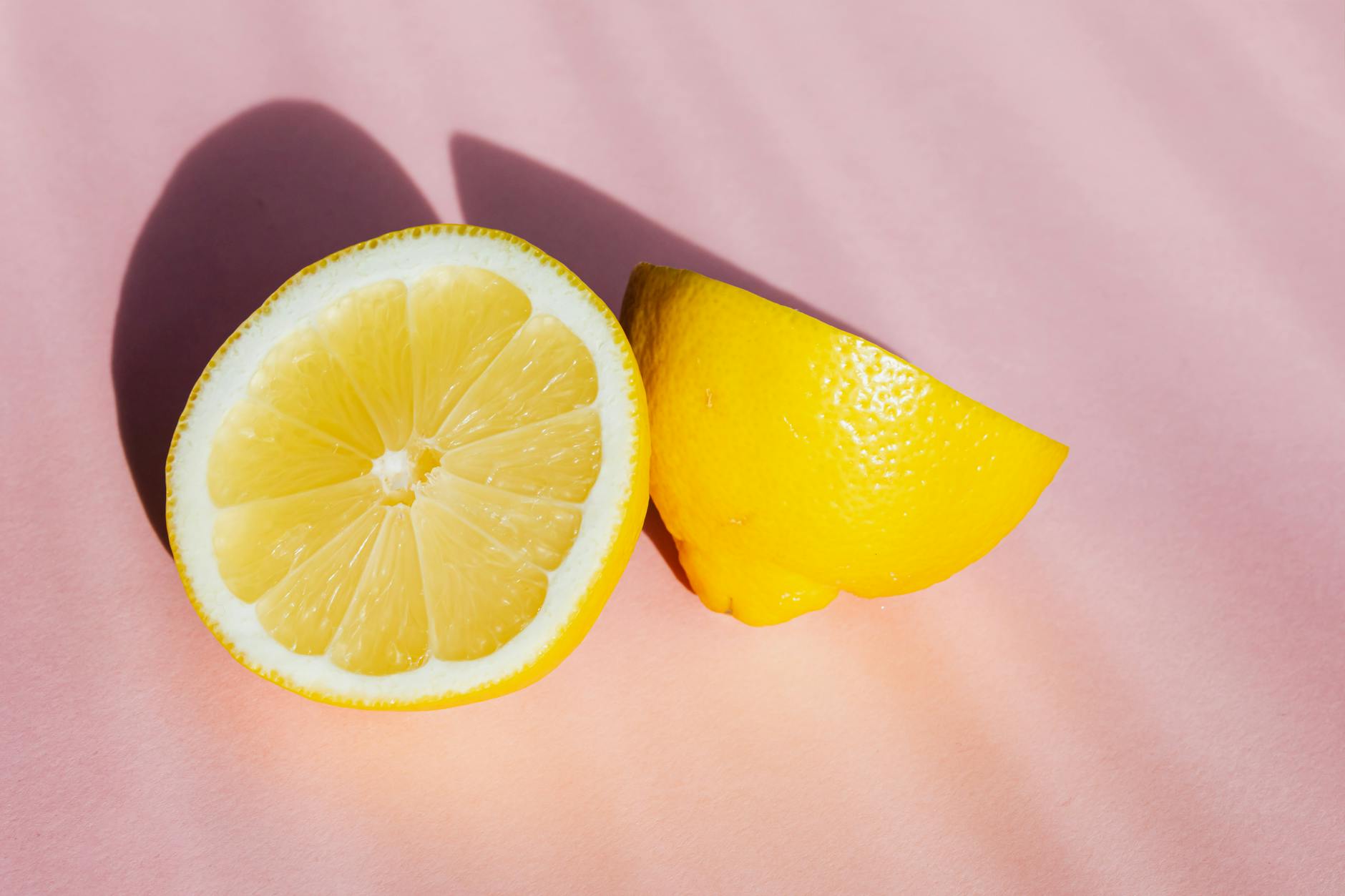 Fresh lemon halves in sunlight on a pink background, symbolizing renewal and vitality