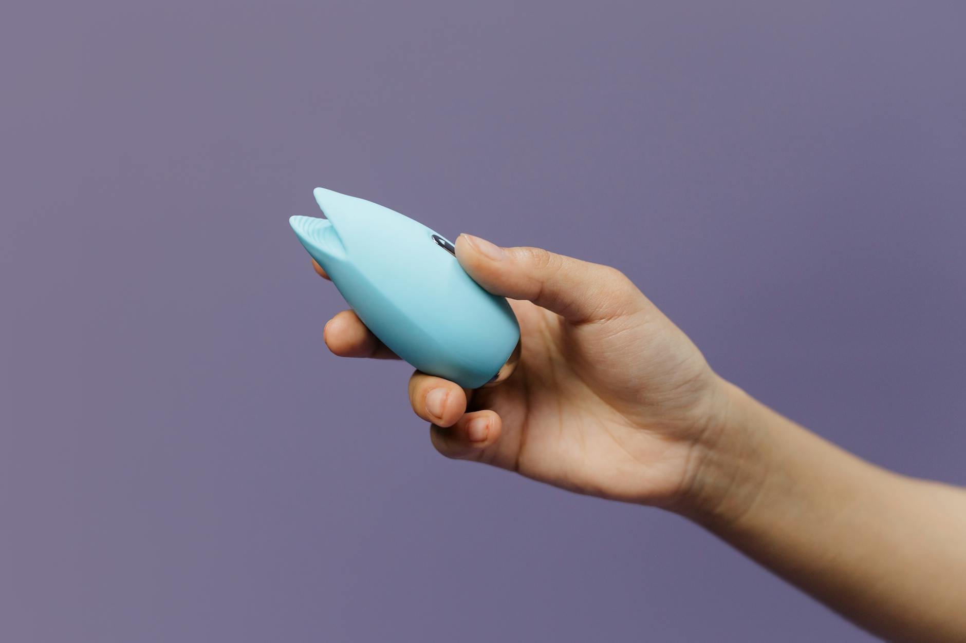 A blue silicone vibrator held in hand against a solid purple background, promoting self-care and pleasure during hormonal changes