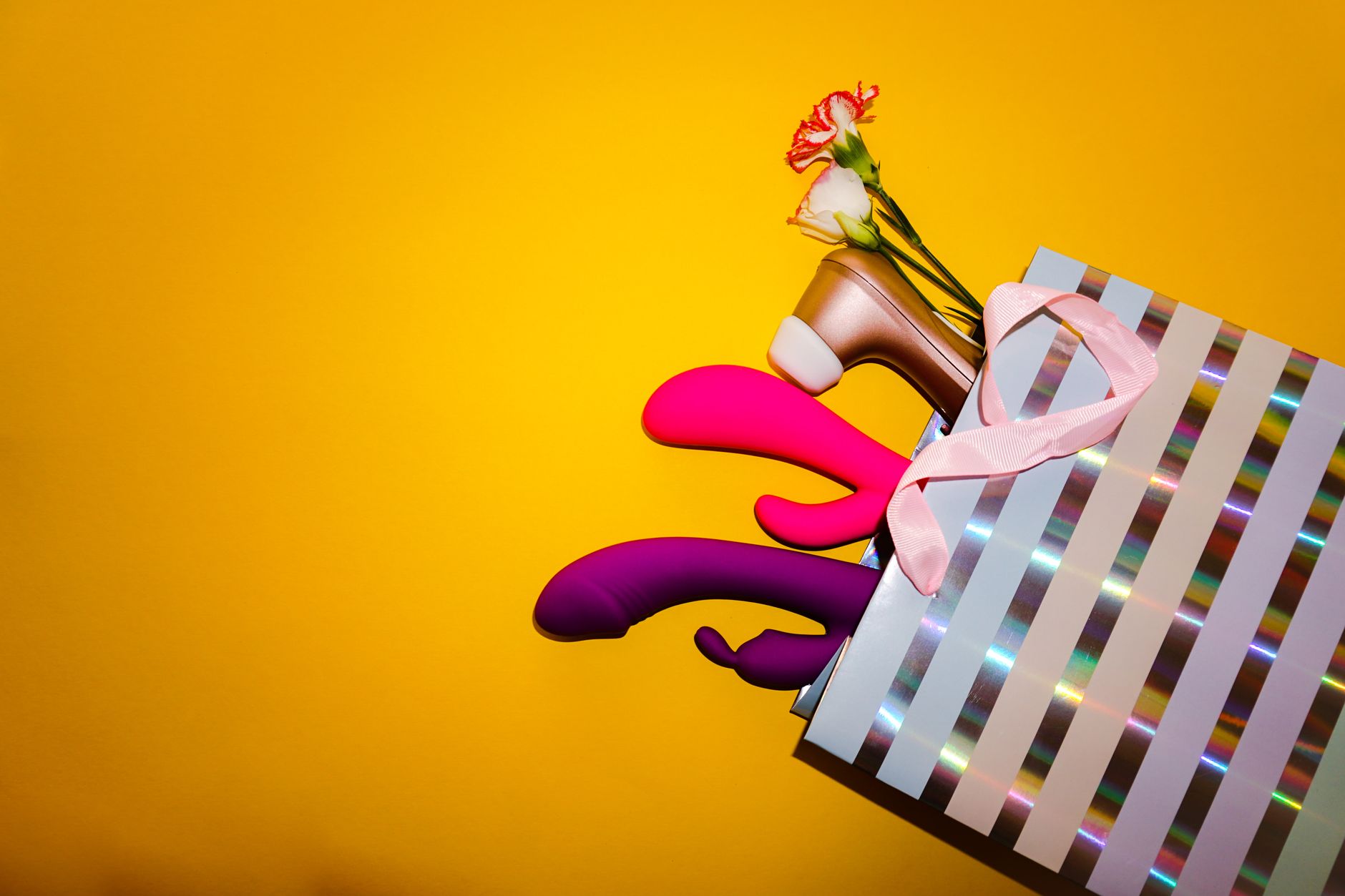Colorful lemon clitoral vibrators and other adult toys in a gift bag on a bright yellow background.