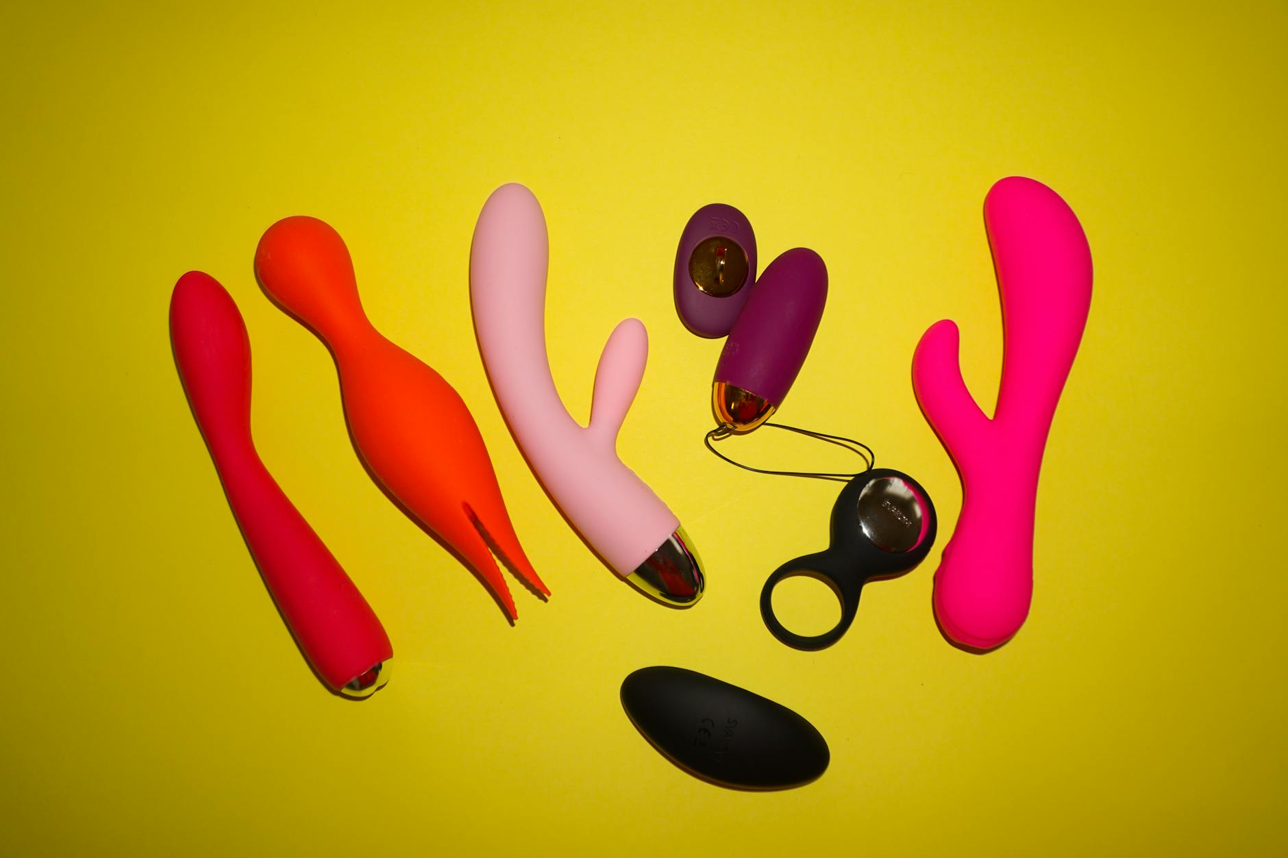 Two hands holding silicone vibrators in different colors against a pastel background